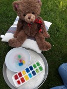Ein Teddybär sitzt vor einem Malkasten