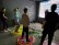 Vier Schüler*innen stehen auf bunten Kreisen vor einer Gaming-Leinwand.