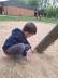 Ein Junge kniet im Sand neben dem Klettergerüst und findet unter dem Gerüst ein gelbes Osterei. 
