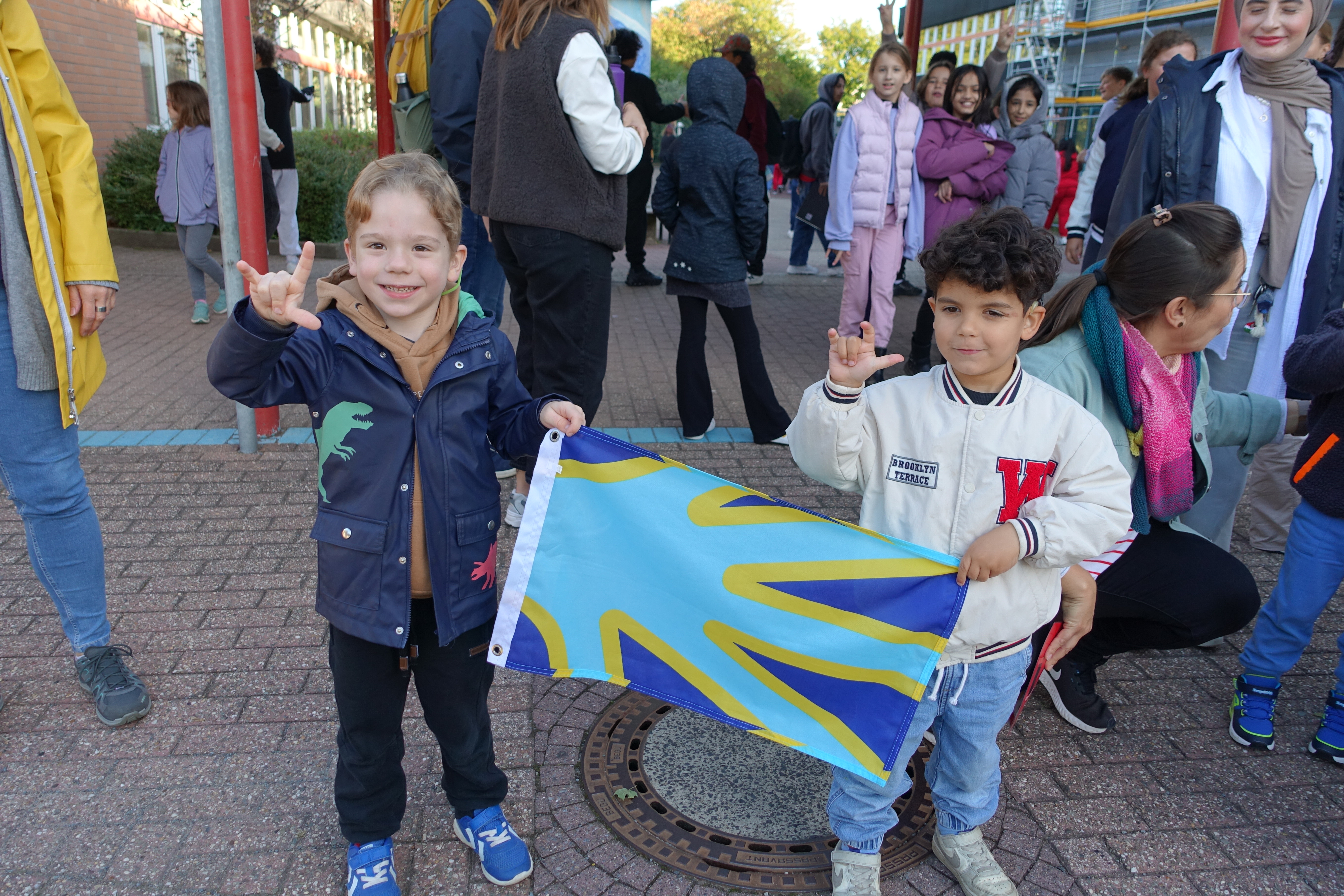 Zwei Kindergartenkinder halten die Flagge, dahinter viele Menschen