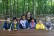 6 Kinder sitzen mit einer Lehrerin an einem Holztisch im Wald.