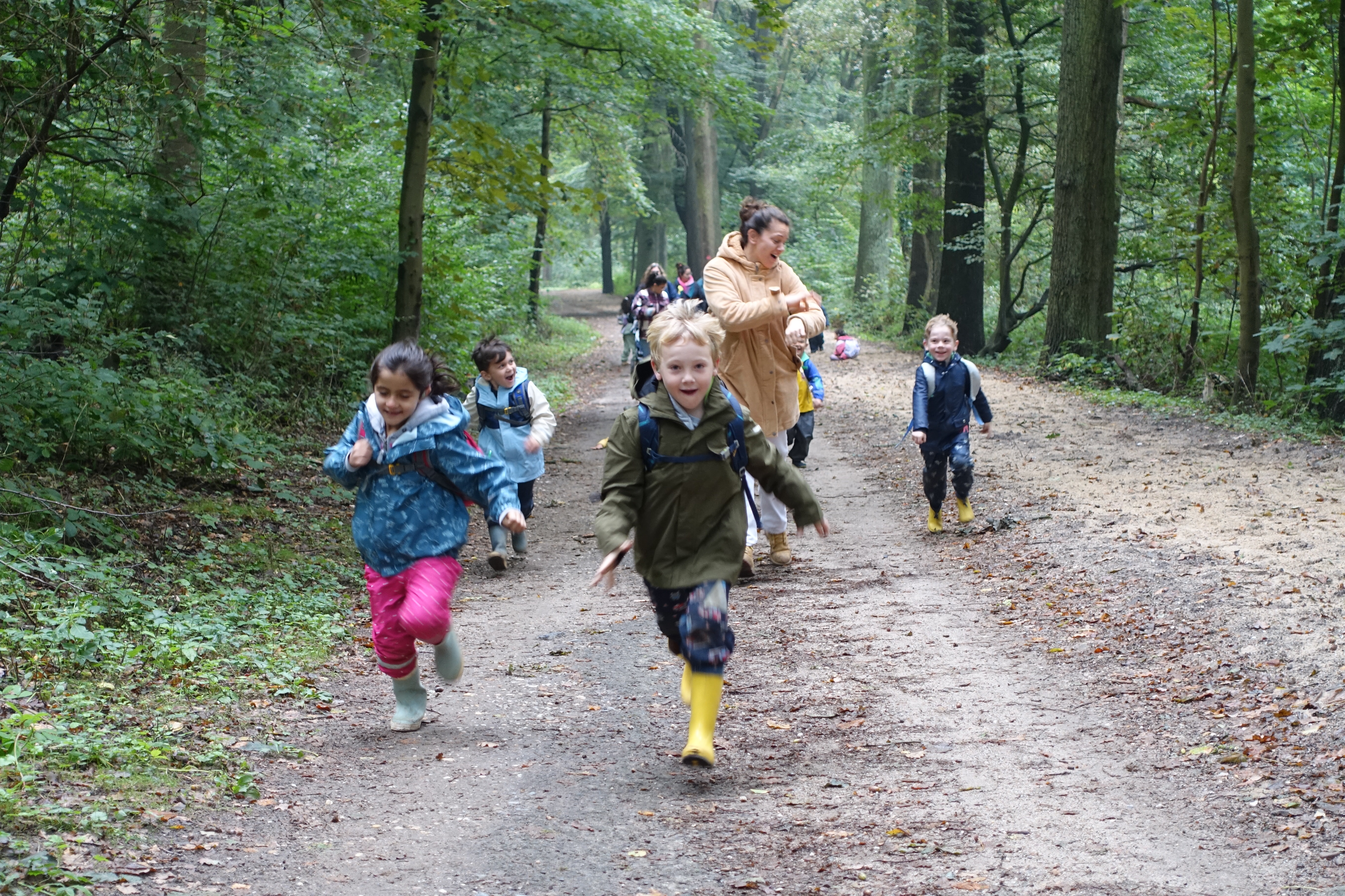 mehrere Kinder rennen einen Waldweg entlang und lachen