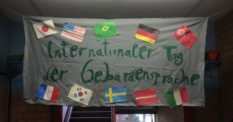 Graues Banner mit der Aufschrift "Internationaler Tag der Gebärdensprache" und den Flaggen von verschiedenen Ländern