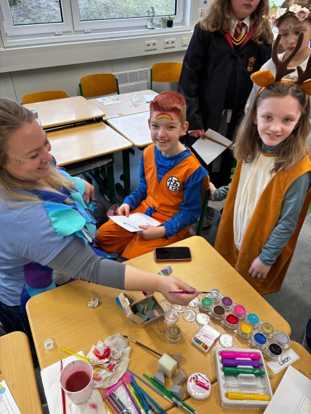 Ein Kind wird von einer Lehrerin geschminkt, andere verkleidete Kinder stehen dabei