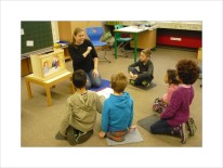 Grundschulkinder und eine Lehrerin sitzen auf dem Boden mit einem Kamishibai