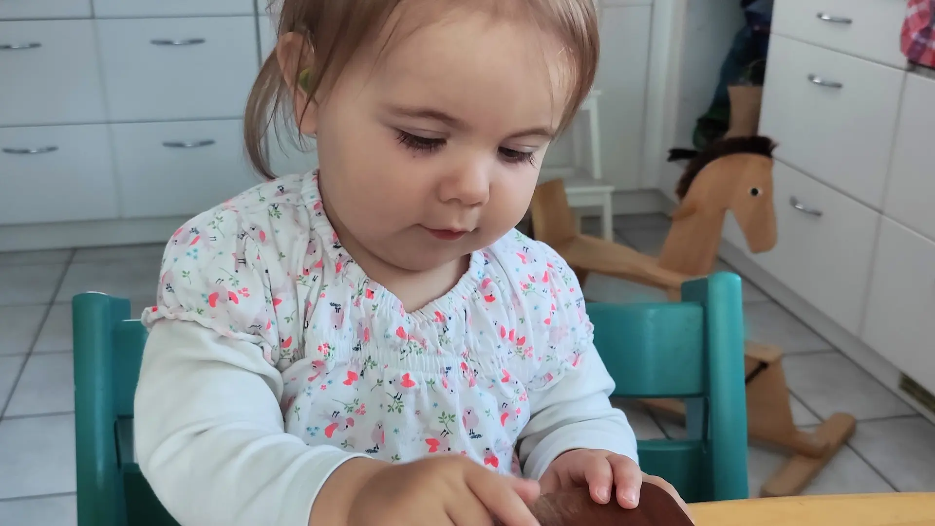 Kleines Kind sitzt am Küchentisch und macht mit einem Daumenklavier Musik