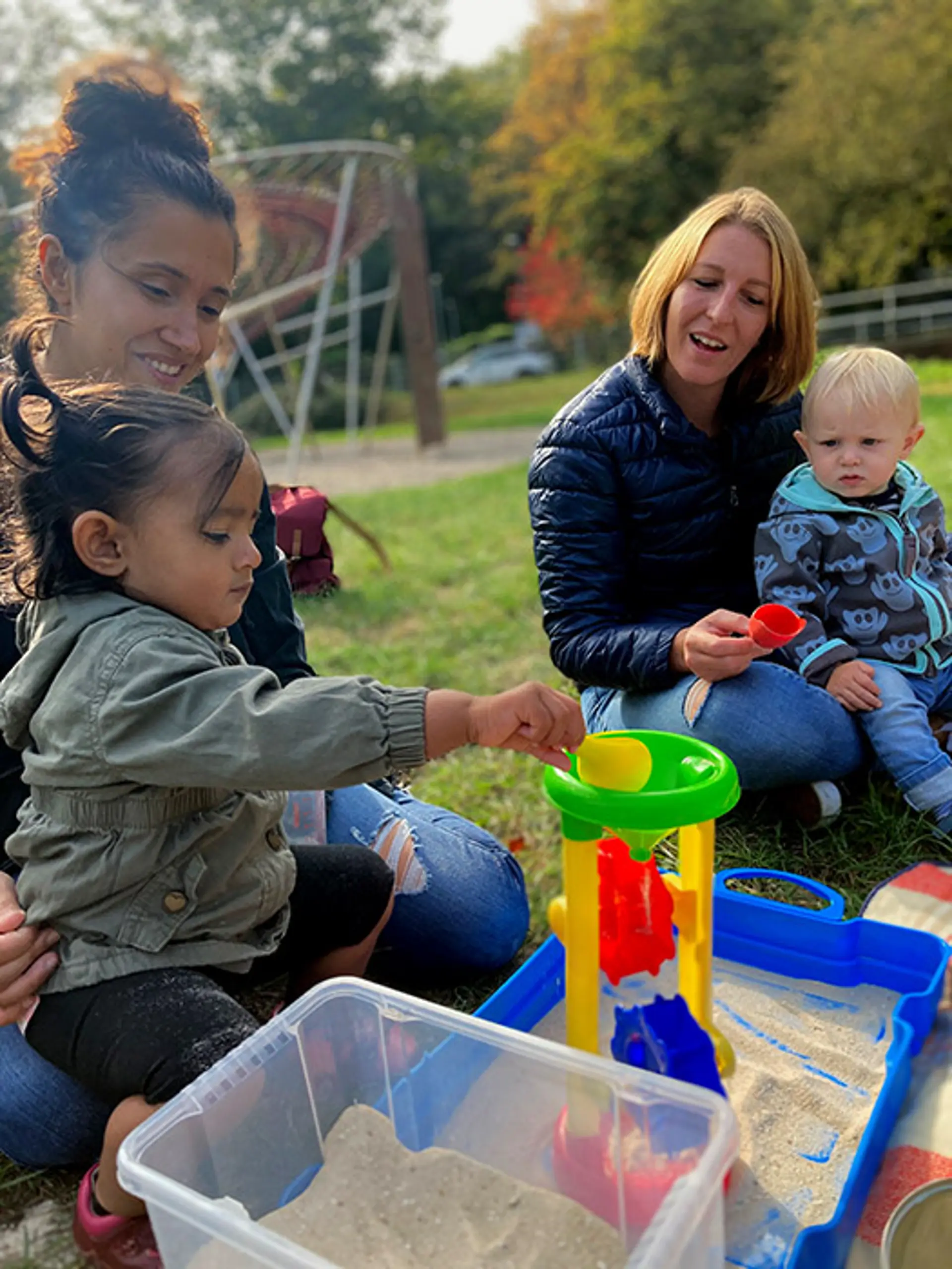 Kinder der Frühförderung spielen mit Sand und sitzen mit Erwachsenen auf dem Boden