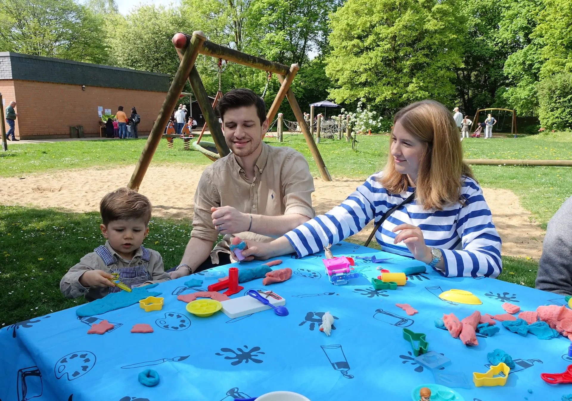 eine Familie sitzt draußen an einem Tisch und spielt mit Knete