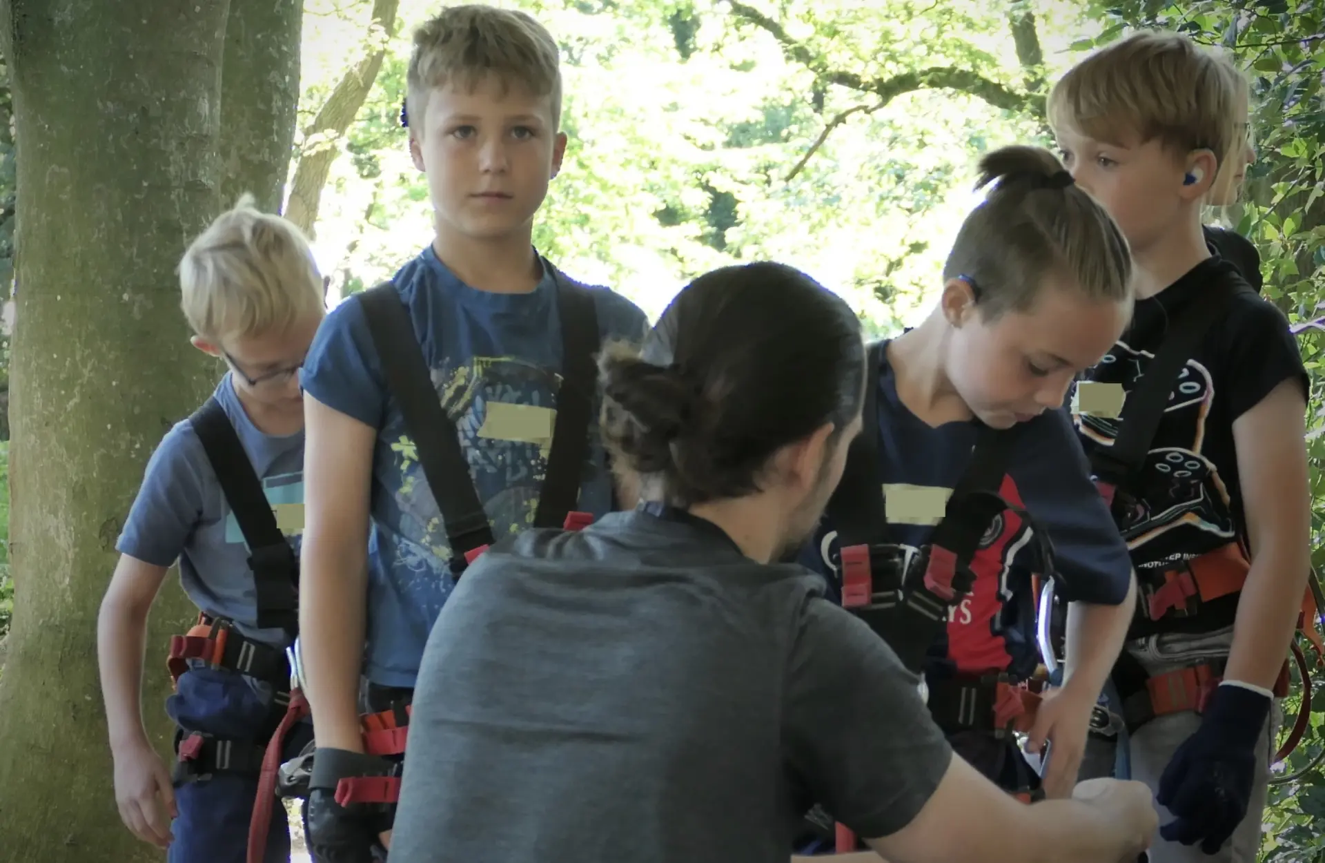 Mehrere Kinder werden zum Klettern im Hochseilgarten von einer Fachkraft gesichert