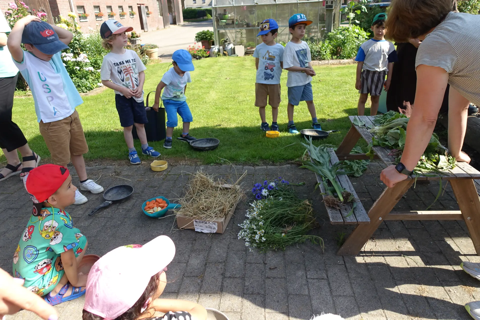 Kinder stehen mit leeren Schüsseln vor unterschiedlichen geernteten Pflanzen und geschnittenem Gemüse