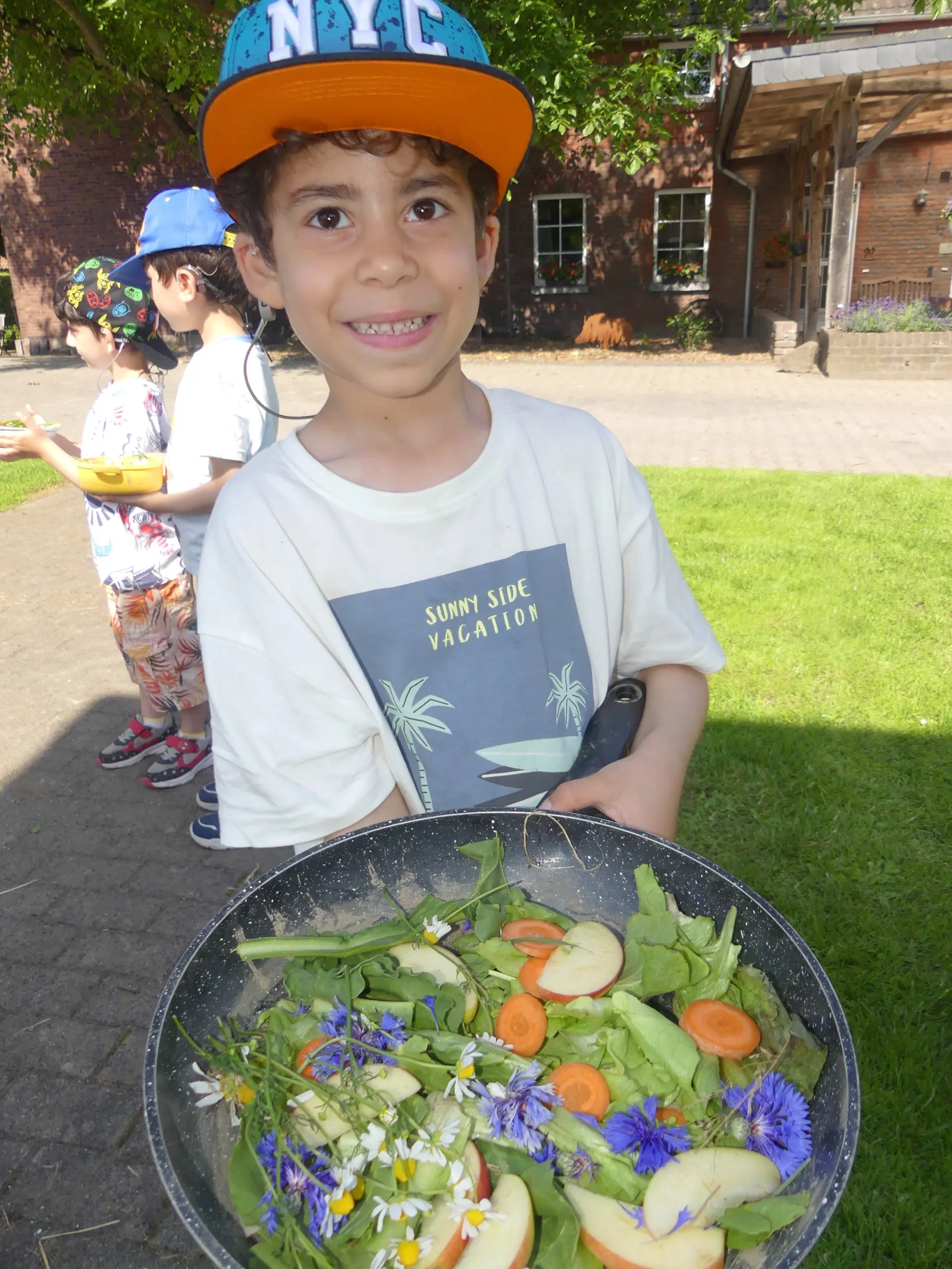 ein Kind hält eine Pfanne mit Pflanzen und geschnittenem Gemüse darin