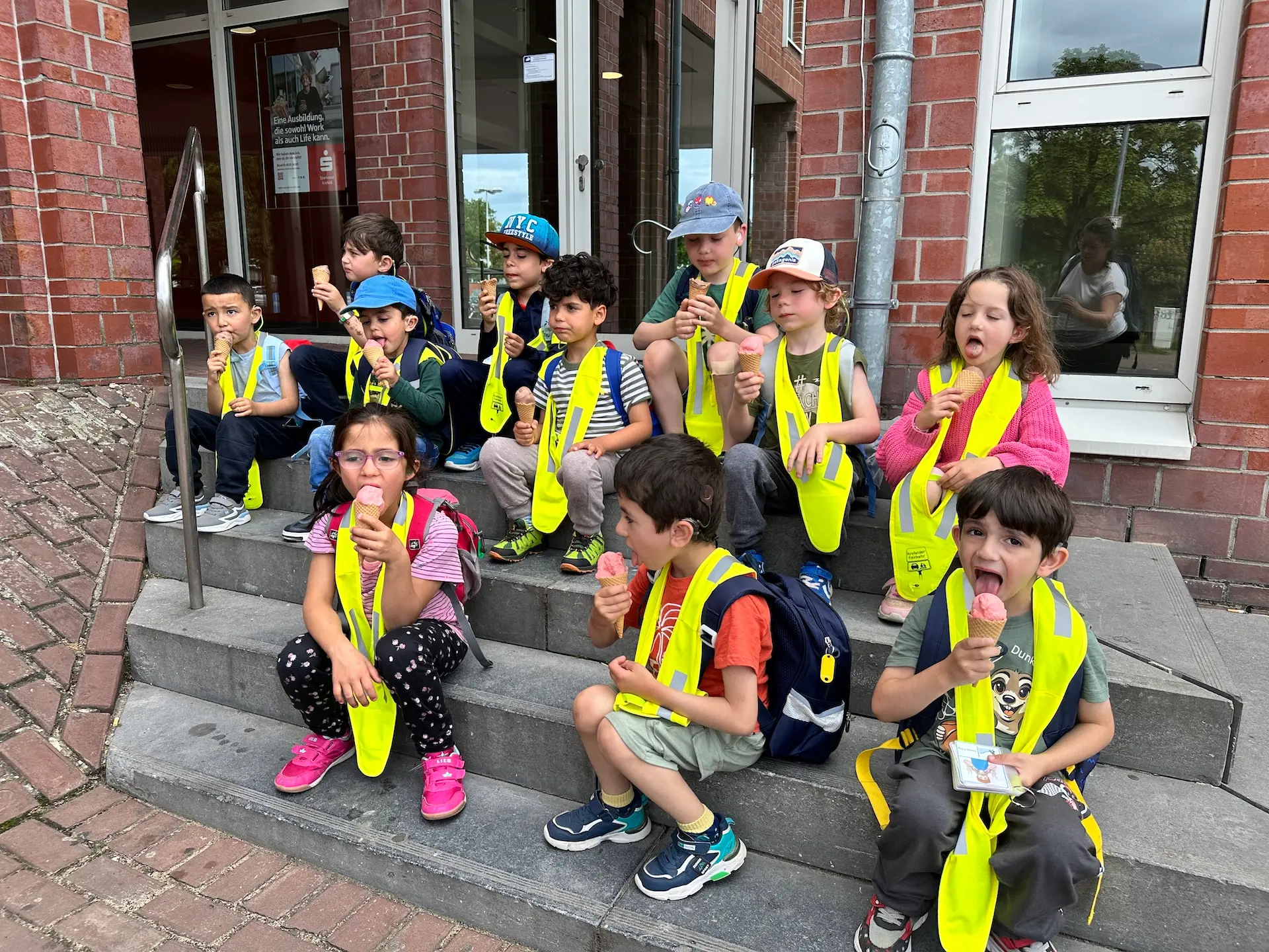viele Kinder sitzen mit gelben Westen auf einer Treppe und essen Eis