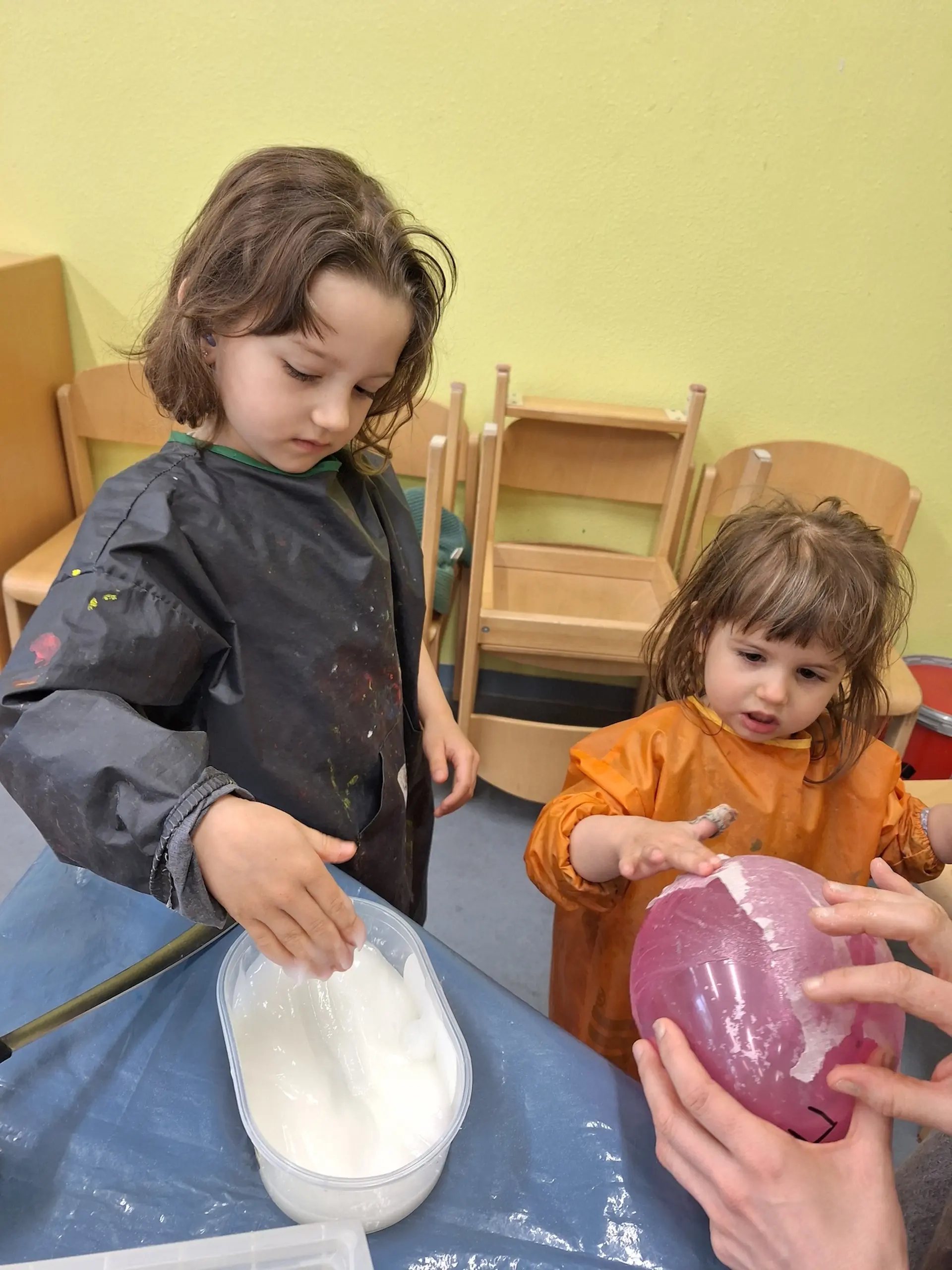 Zwei Kinder tragen mit ihren Händen Kleister auf einen Luftballon auf