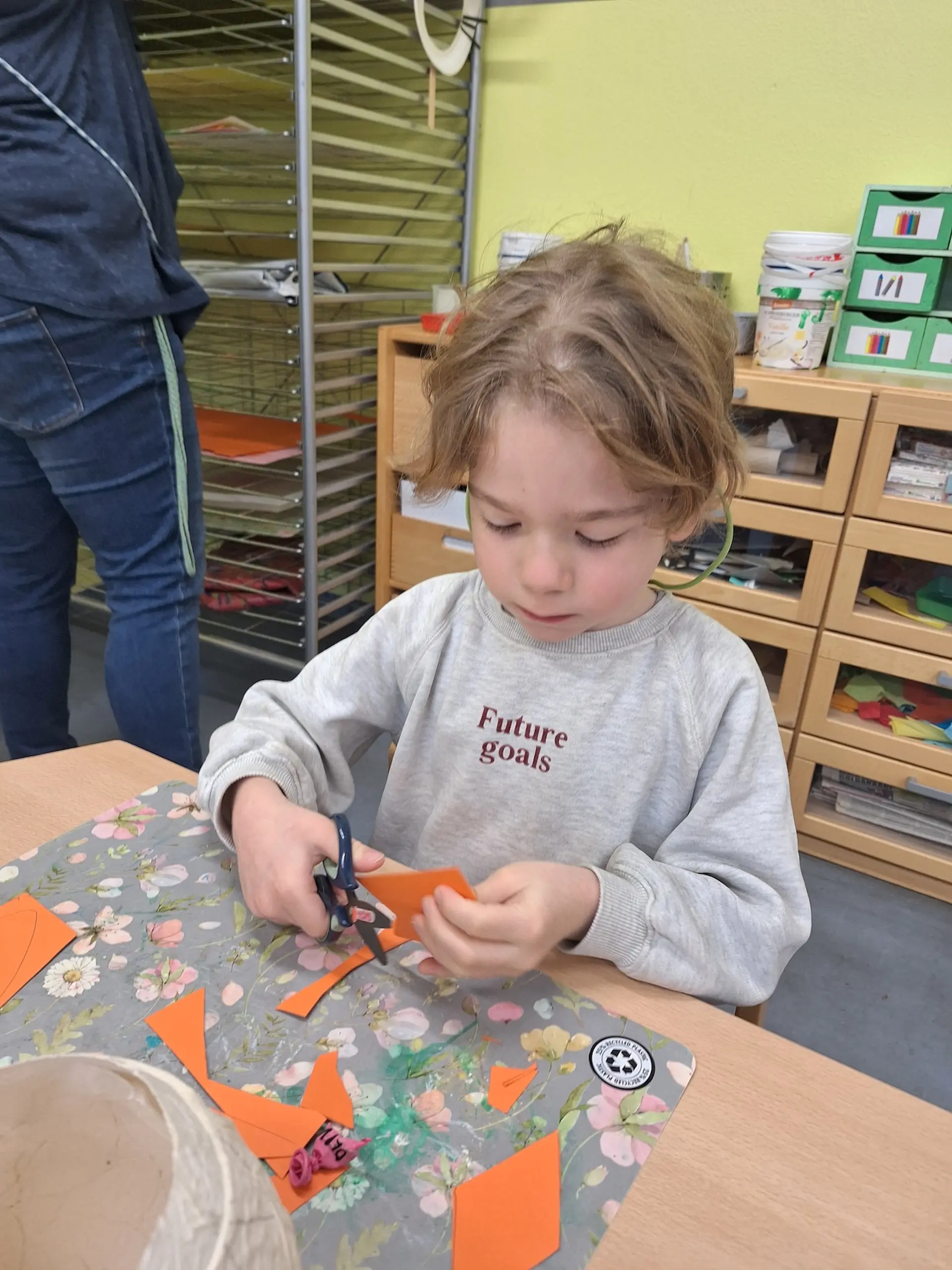 ein Kind schneidet einen Schnabel aus orangener Pappe aus