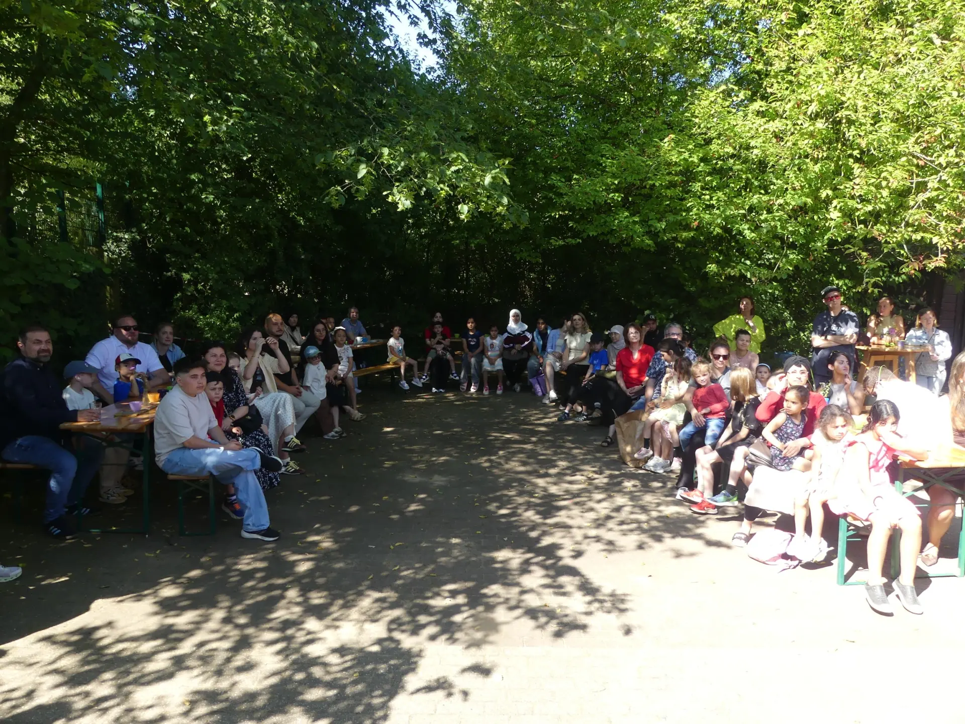Viele Menschen sitzen im Halbkreis unter einem Baum