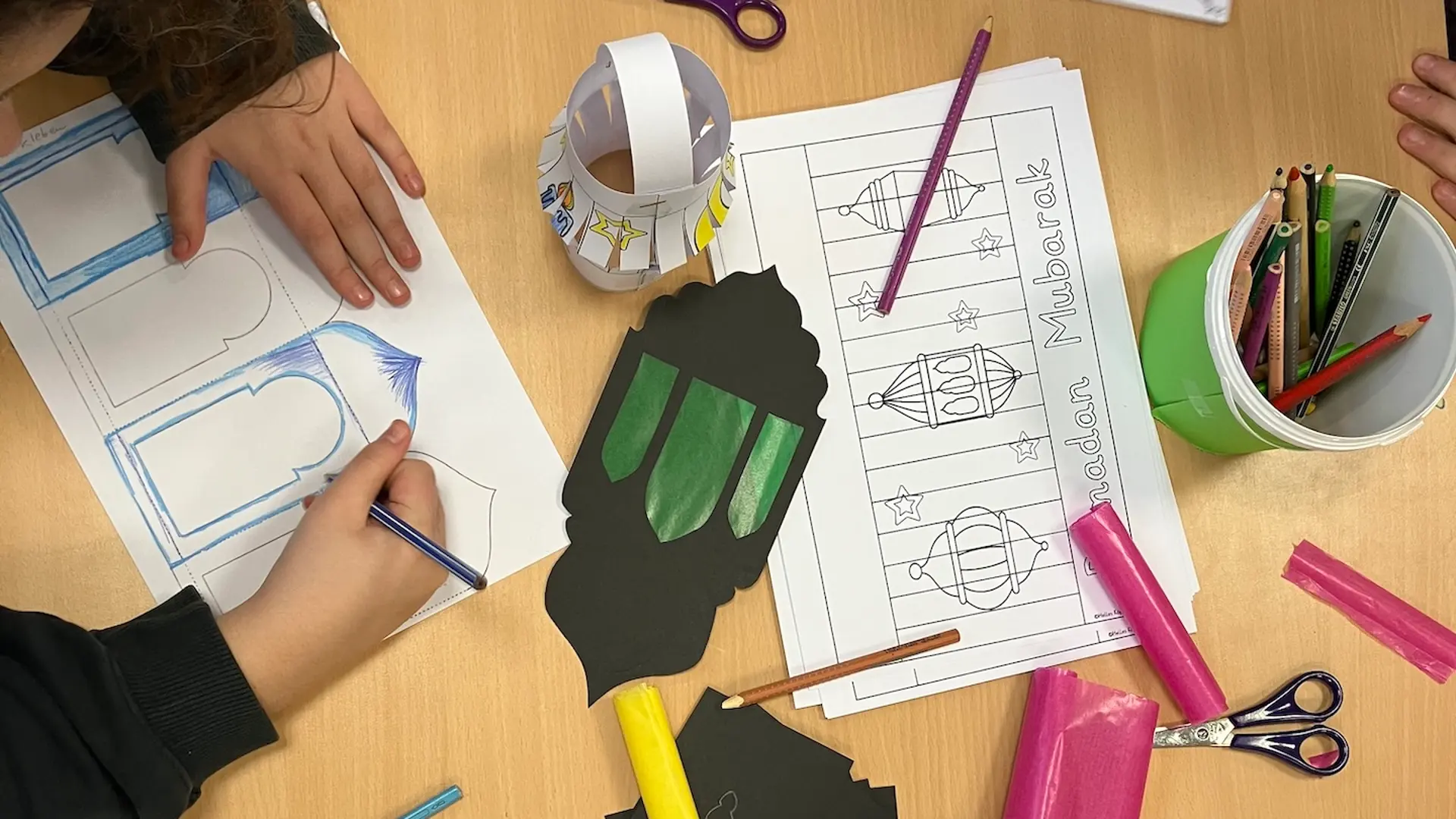 auf einem Tisch sieht man Hände, Bastelmaterial und eine fertige Ramadanlaterne