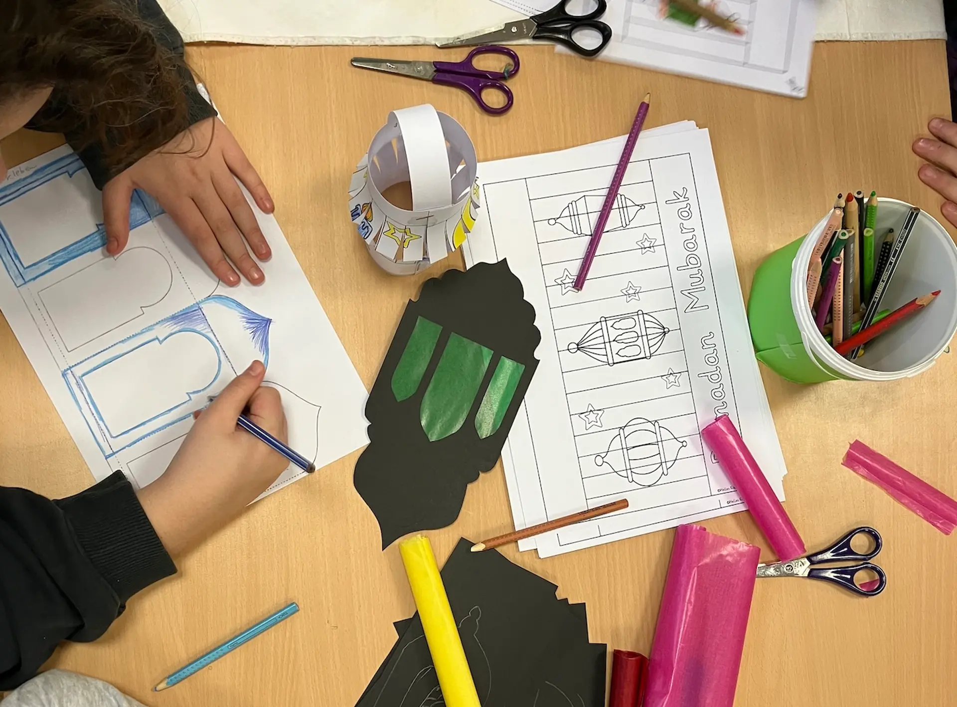 auf einem Tisch sieht man Hände, Bastelmaterial und eine fertige Ramadanlaterne