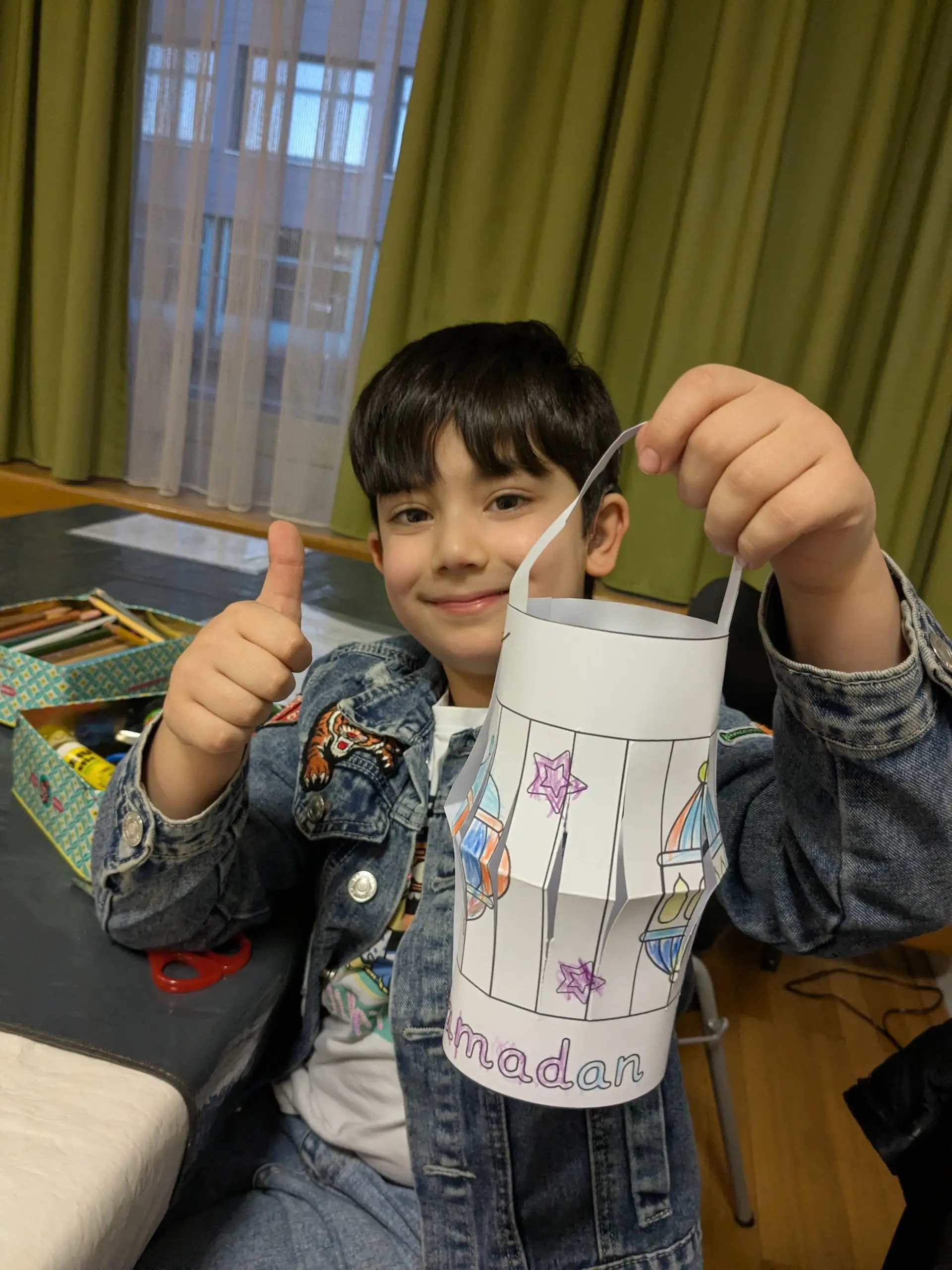 ein Junge hält eine fertig gebastelte Ramadanlaterne und hält einen Daumen hoch