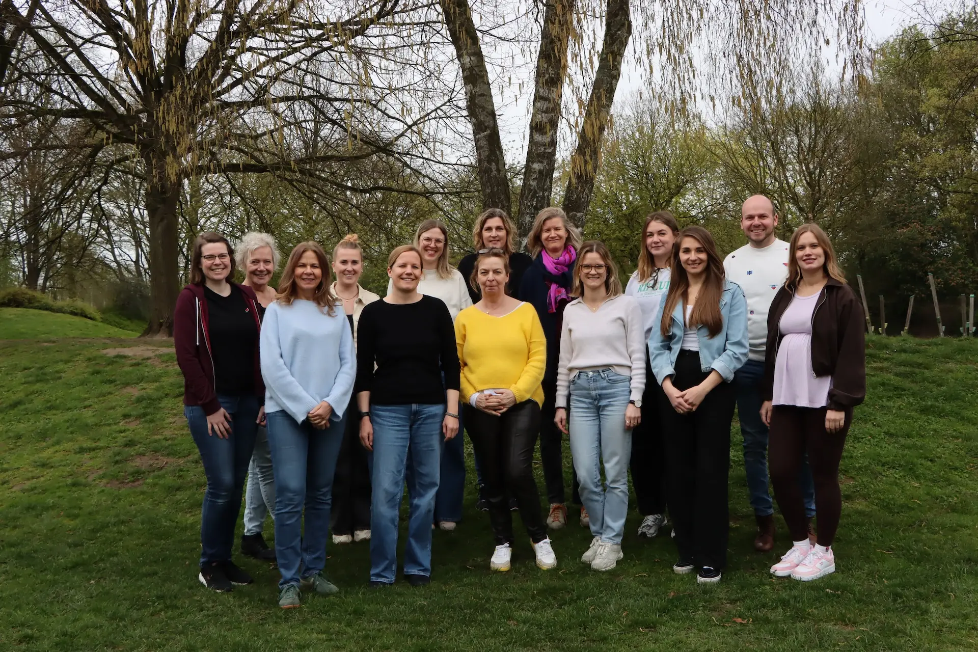 12 Lehrerinnen, 1 Lehrer und die Schulleiterin stehen auf einer Wiese auf dem Schulhof