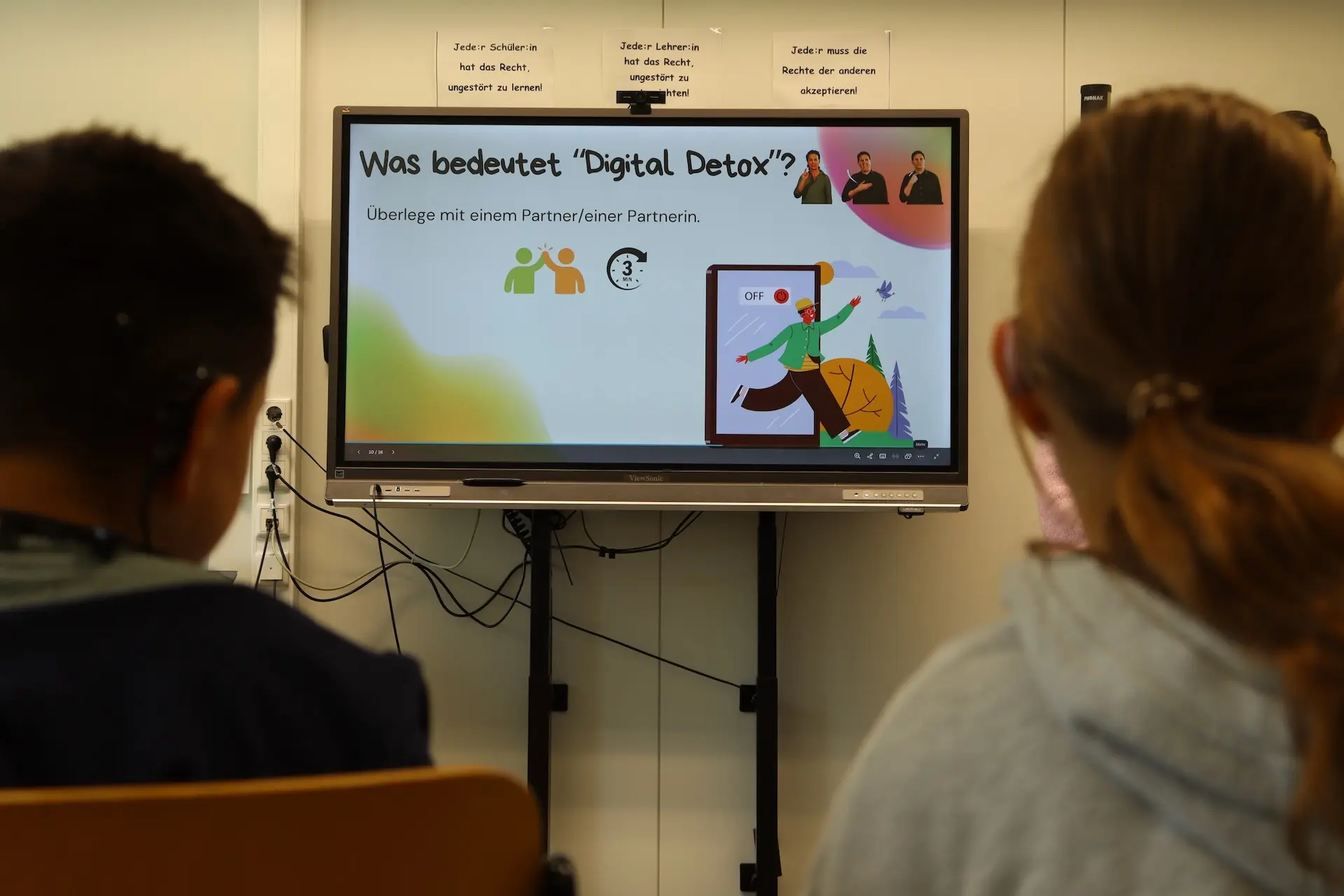 2 Schüler*innen schauen auf eine digitale Tafel mit der Überschrift "Was bedeutet Digital Detox?"