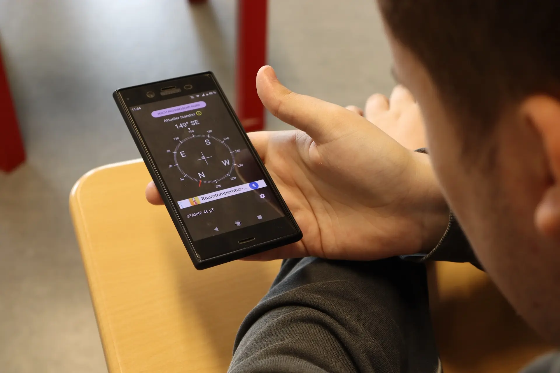 Ein Handy mit geöffneter Kompass-App liegt in einer Schüler-Hand