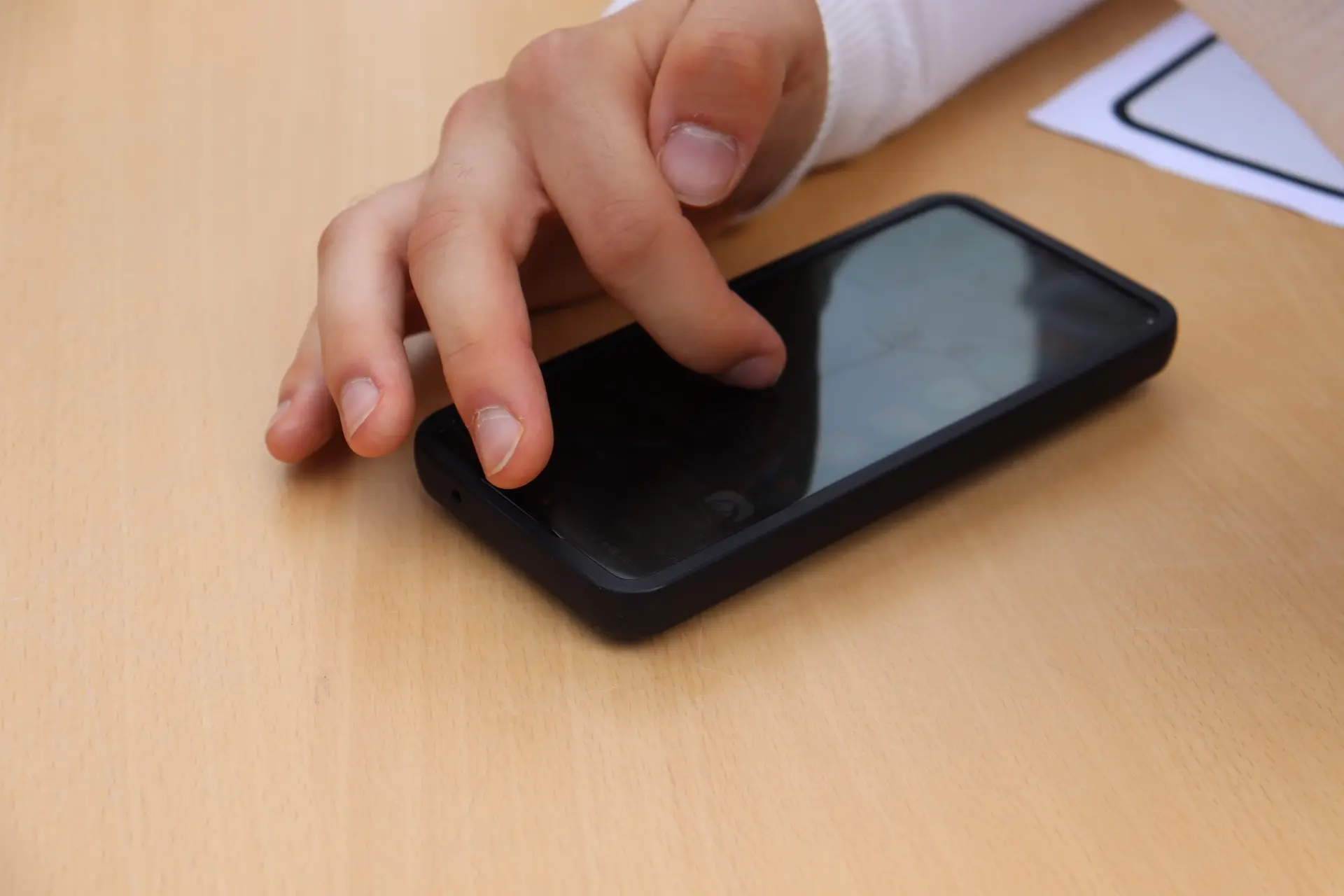 Ein Handy liegt auf einem Tisch, eine Hand wischt auf dem Handy