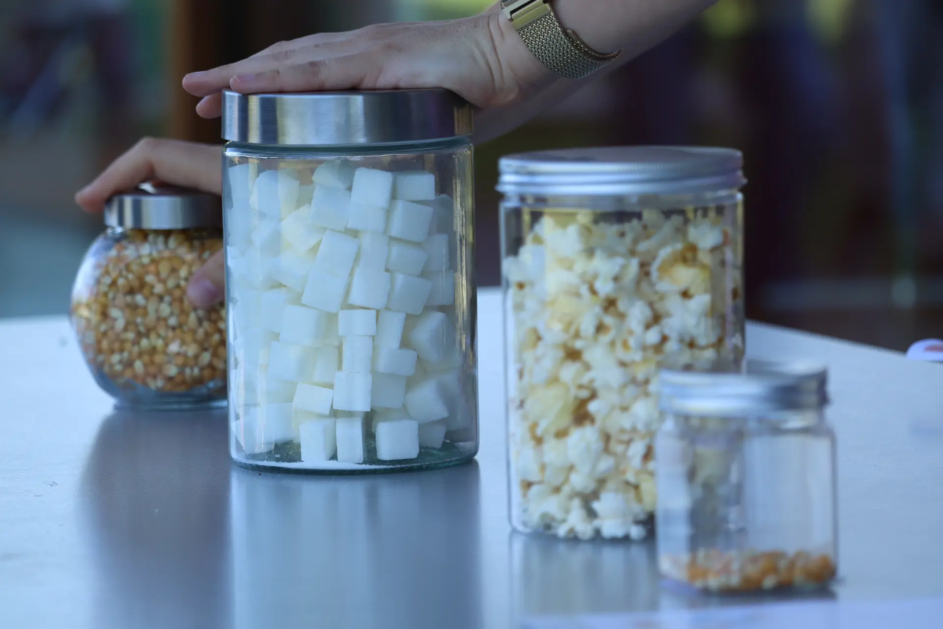 Schulfahrt: Mengen schätzen – vier Gläser mit Inhalten wie Popcorn, Zuckerwürfel und Maiskörnern stehen auf dem Tisch