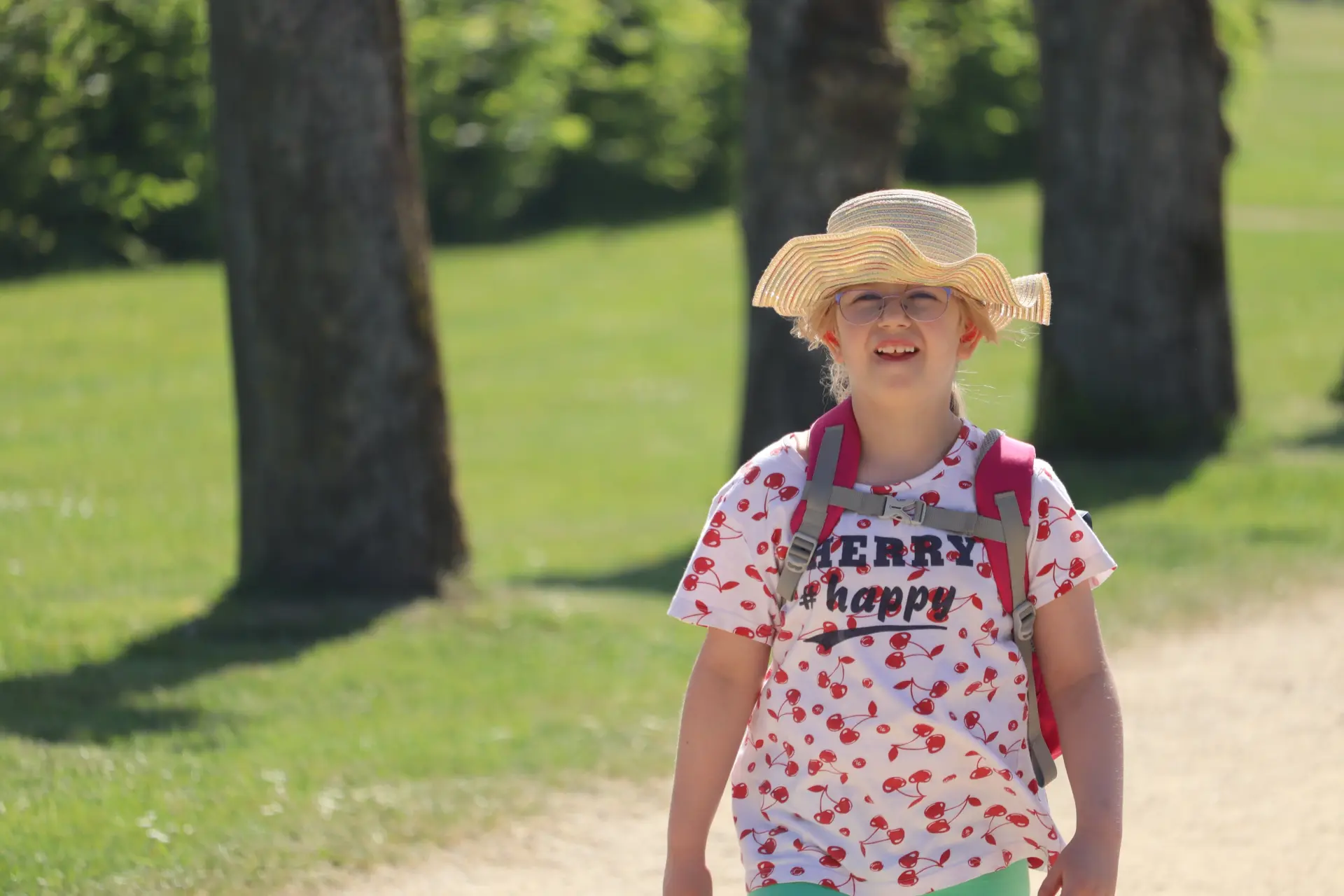 Schulfahrt: Kind mit Sonnenhut geht Parkweg entlang