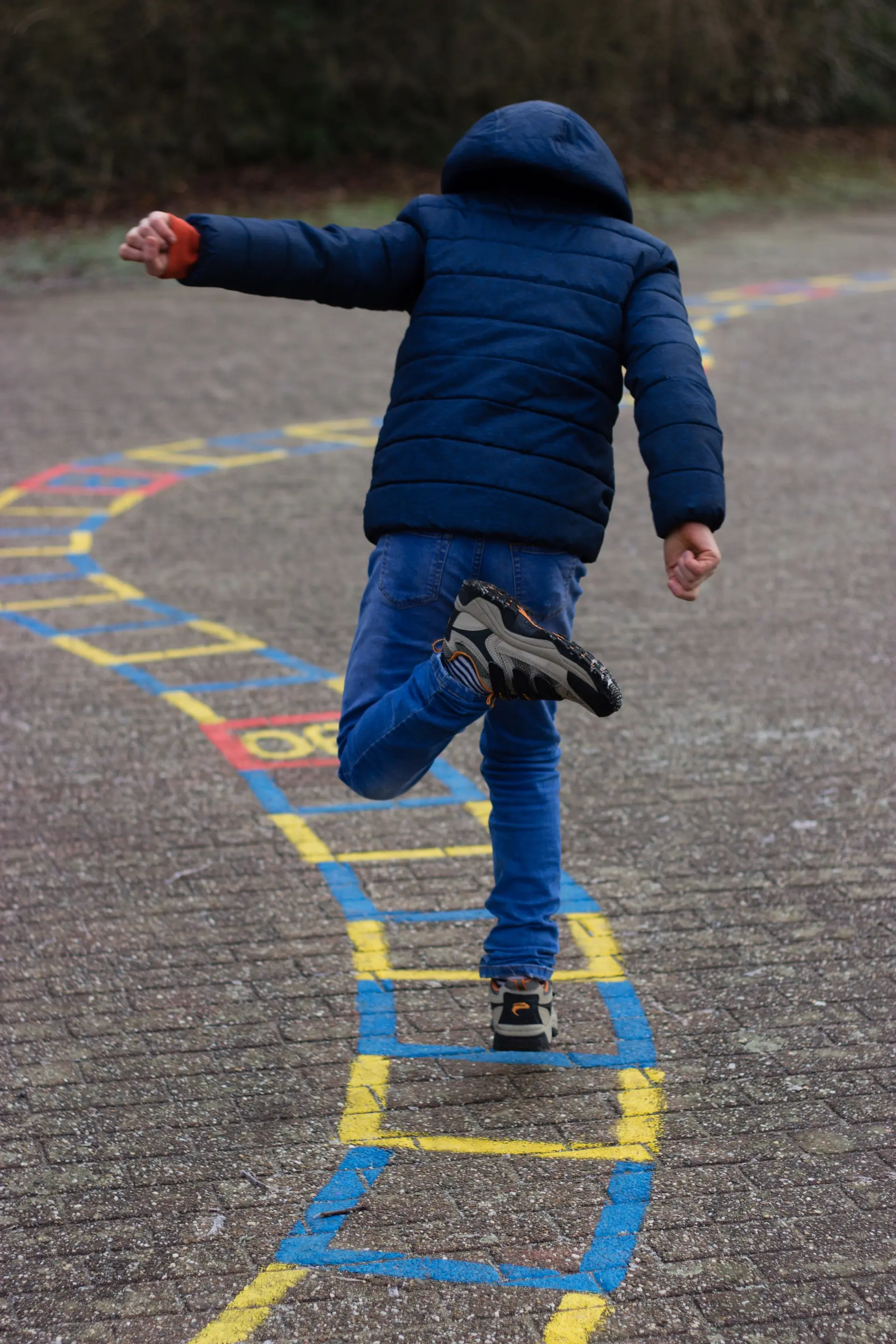 Kind springt auf dem Schulhof durch ein aufgezeichnetes Hüpfekästchen