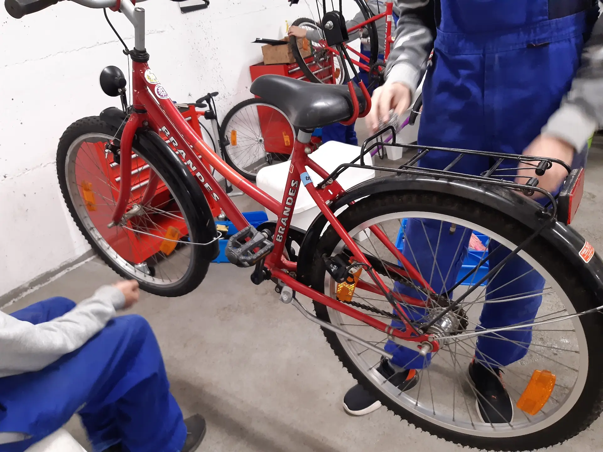Ein rotes Fahrrad wird von zwei Kindern der Fahrradwerkstatt überprüft
