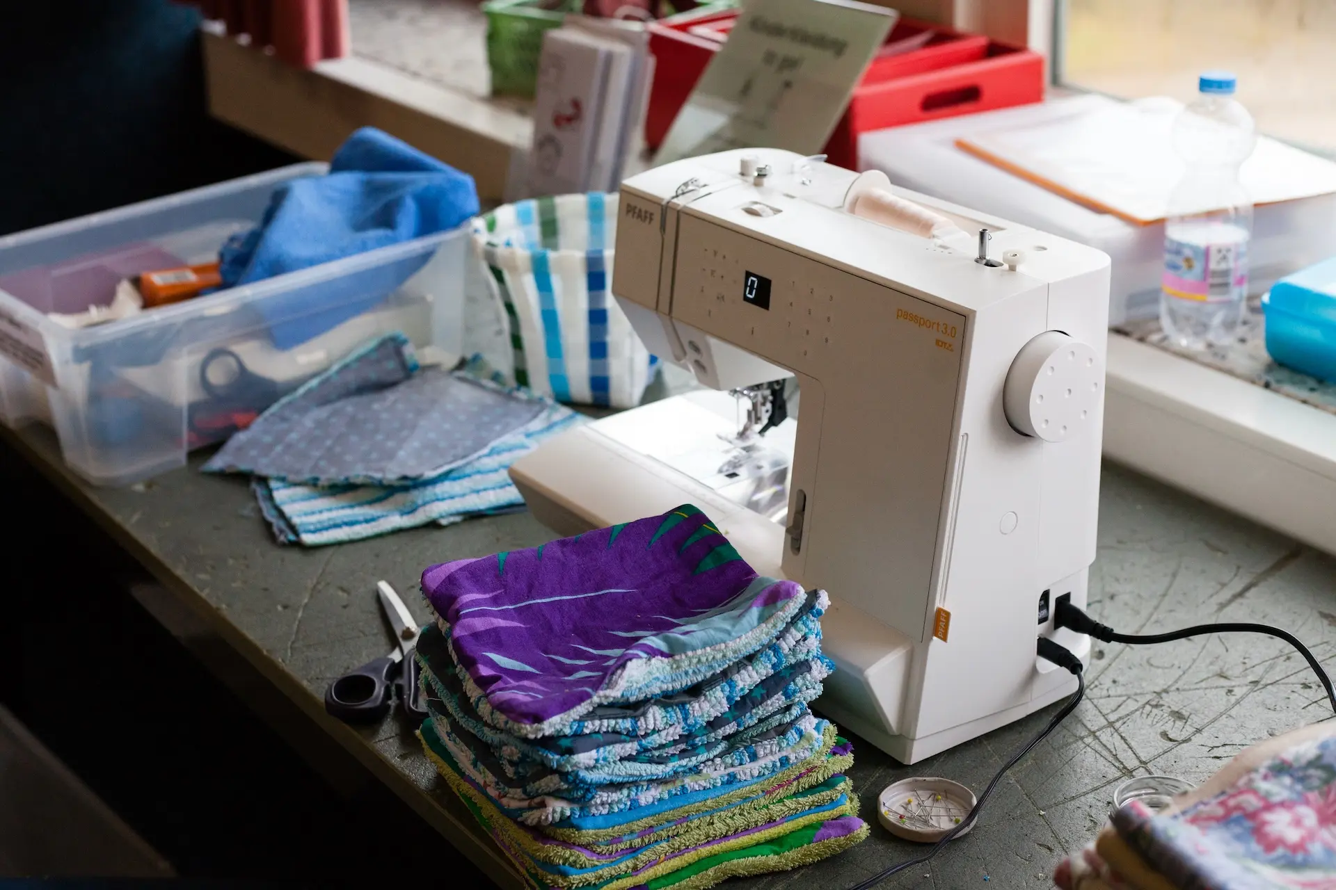 Nähtisch des Second-Hand-Verkauf-Teams: verschiedene Stoffe, Materialien und eine Nähmaschine stehen bereit