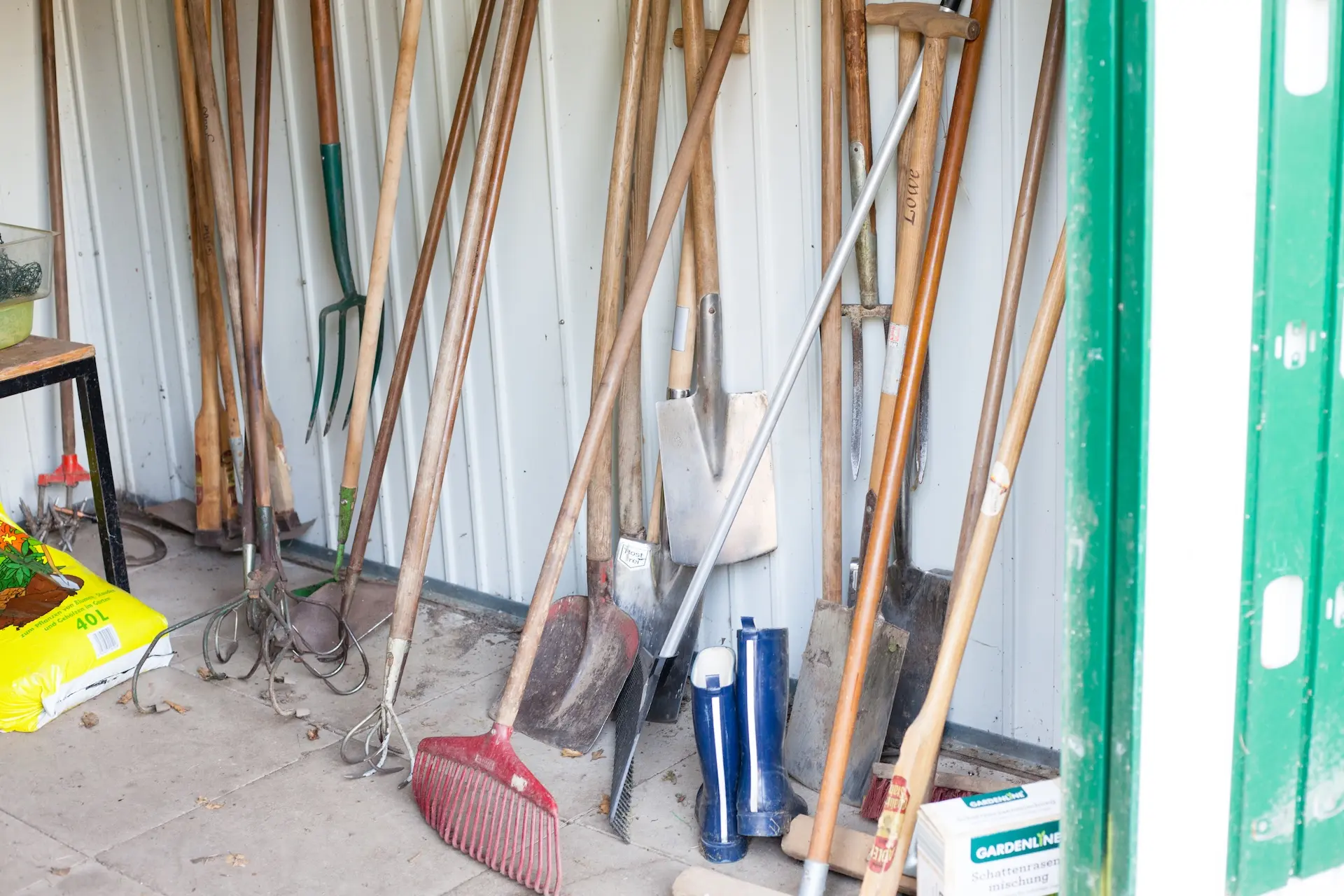 Verschiedene Gartengeräte stehen aufgereiht an der Wand im Schuppen