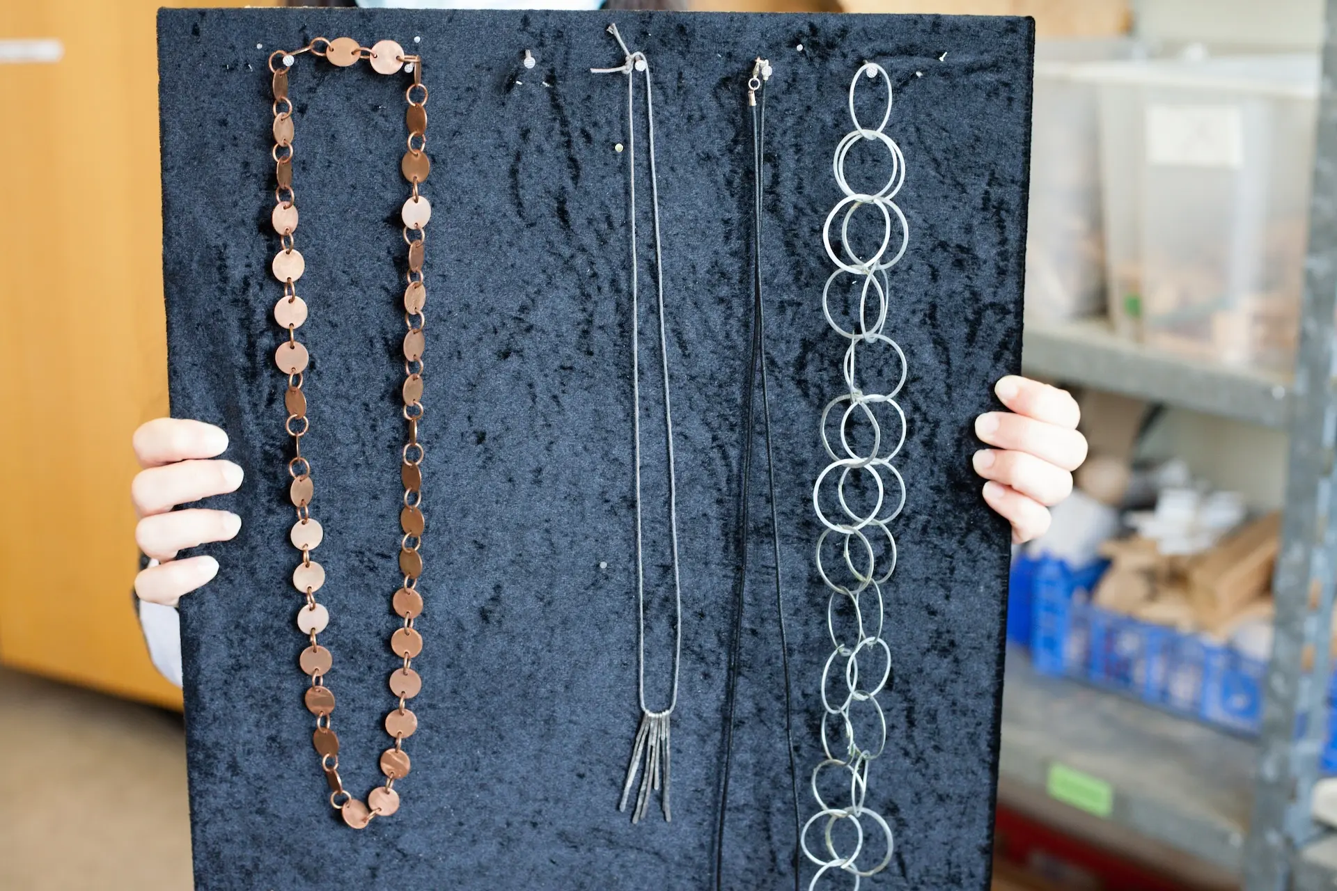 Schüler*in präsentiert fertige Ketten, die auf einem blauen Display ausgestellt sind