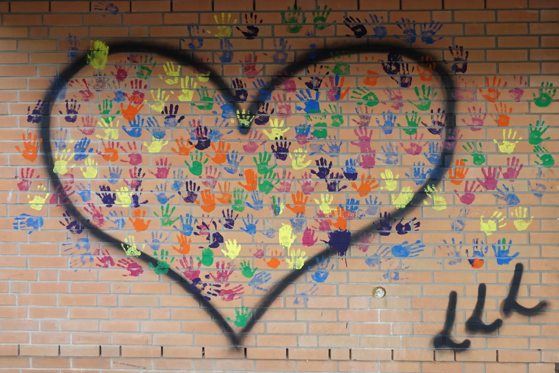 Viele bunte Handabdrücke auf der Hauswand der Schule mit einem gemalten Herzen darum