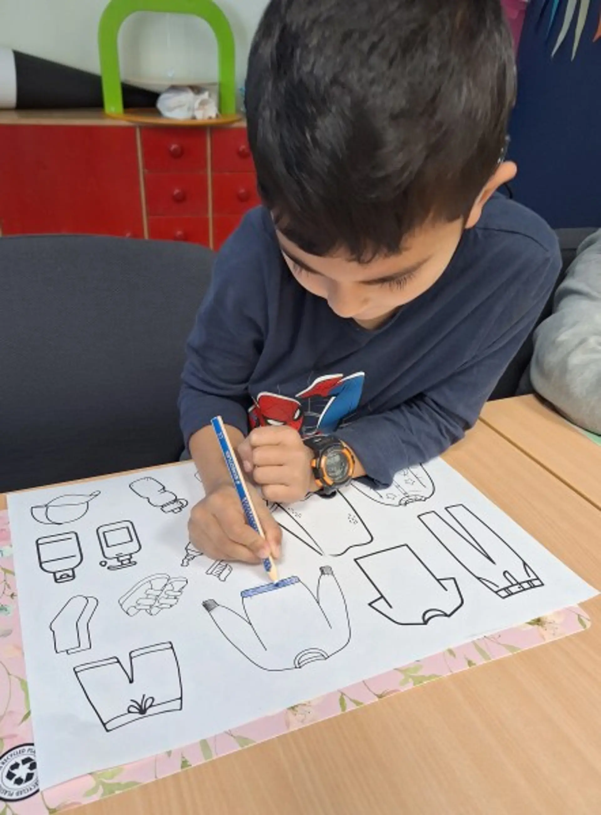 Ein Kind malt verschiedene Kleidungsstücke auf einem Vorlagenblatt aus