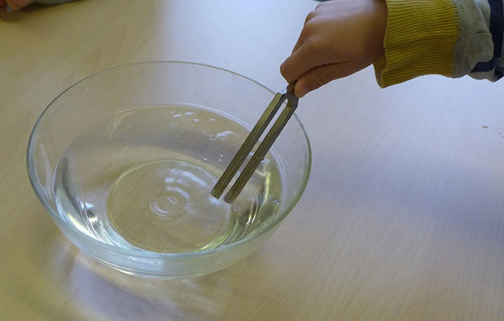 Kind hält Stimmgabel in Wasser, um Schallwellen sichtbar zu machen
